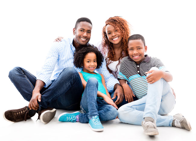 Smiling family sitting together on the floor after visiting Grins & Giggles Family Dentistry in Spokane Valley, WA