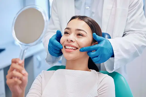 Smiling female dental patient looking into mirror and smiling with healthy teeth at Grins & Giggles Family Dentistry in Spokane Valley, WA