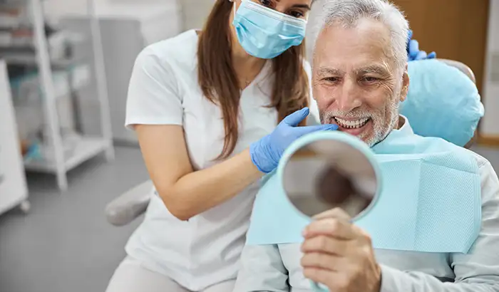 Older man sitting on dental chair and holding up a mirror to his new and restored smile with dental implants by Grins & Giggles Family Dentistry in Spokane Valley, WA Older man sitting on dental chair and holding up a mirror to his new and restored smile with dental implants by Grins & Giggles Family Dentistry in Spokane Valley, WA