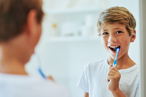Young boy looking at mirror and brushing his teeth after learning brushing and flossing tips from Grins & Giggles Family Dentistry in Spokane Valley, WA