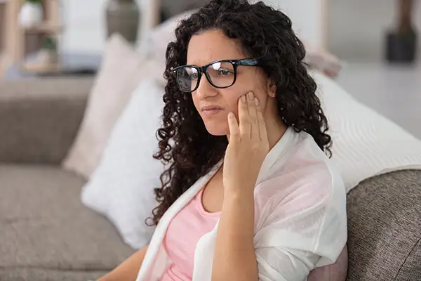 A woman sitting on a couch holding her jaw in pain, showing signs of toothache.
